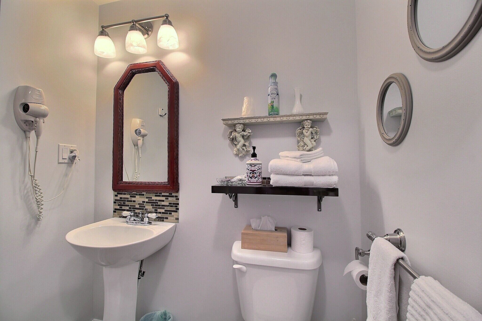 A bathroom with a white sink, a mirror with a wooden frame, a towel rack with towels, and a shelf with toiletries.