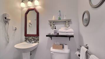 A bathroom with a white sink, a mirror with a wooden frame, a towel rack with towels, and a shelf with toiletries.
