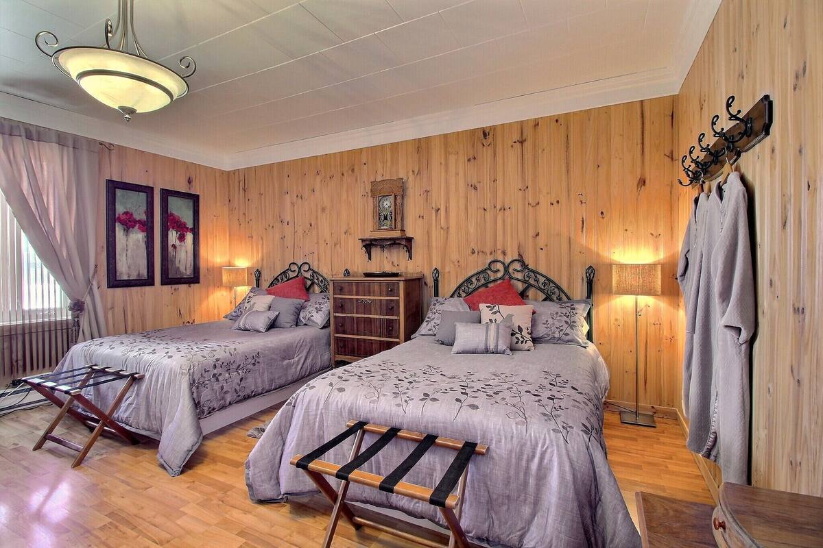 Una habitación con dos camas, paredes de madera, una lámpara colgante y un reloj en la pared.