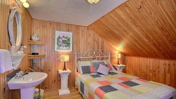 Une chambre à coucher chaleureuse avec des murs en bois, un lit recouvert d’une courtepointe colorée, une table de chevet blanche, une lampe blanche et un miroir.