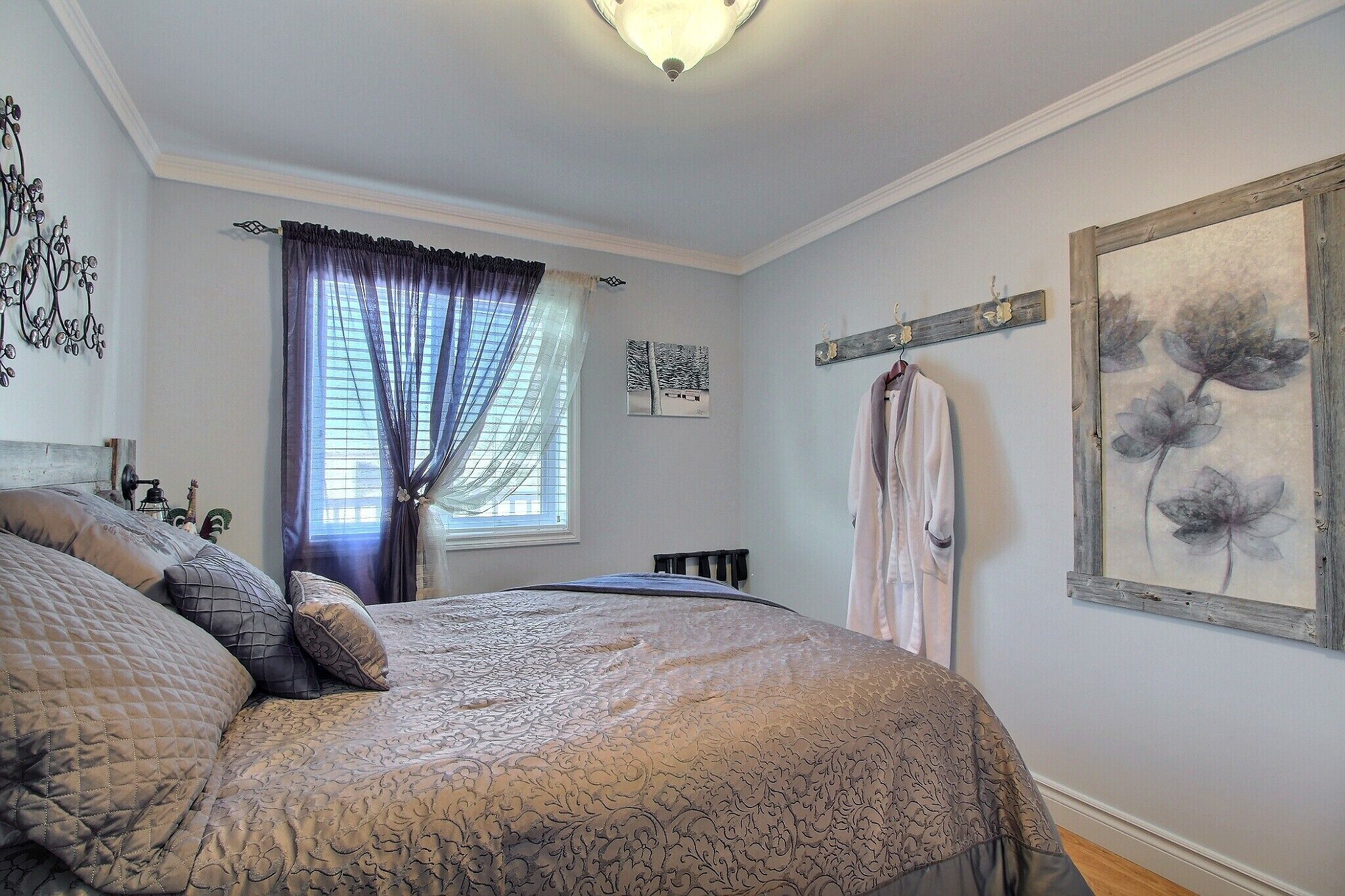 A bedroom with a large bed, a window with curtains, a radiator, and a wall-mounted coat rack.