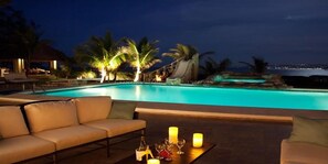 A poolside area with a sofa and candles, palm trees, and a view of the ocean at night. - Seven Seas - Ocho Rios 4BR (Ocho Rios)