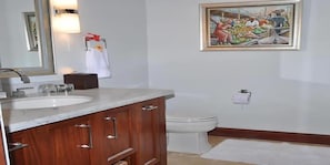 Un baño con tocador de madera, un lavamanos blanco, un inodoro y un cuadro enmarcado en la pared.