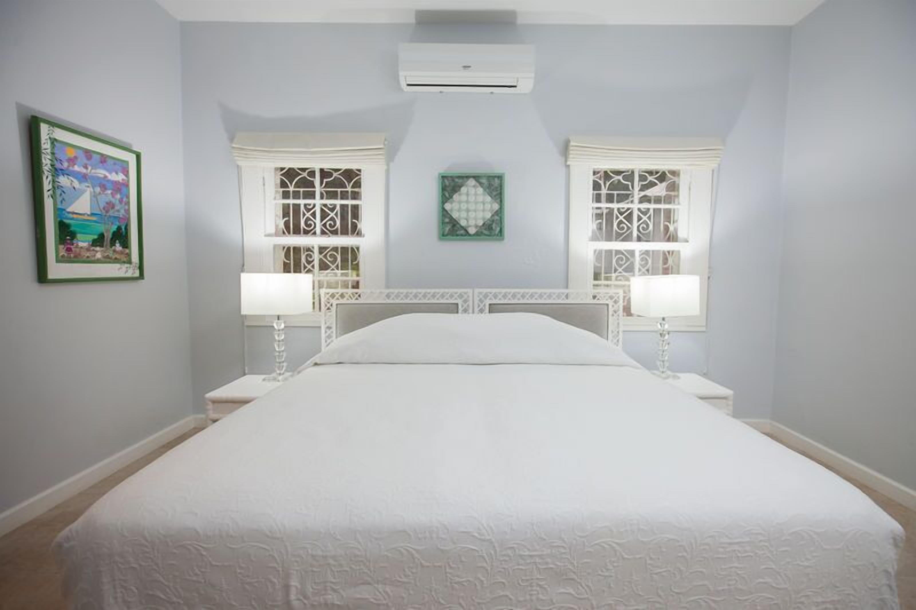 Un dormitorio con una cama grande, dos mesitas de noche y dos ventanas con rejas decorativas.