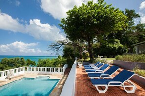 A poolside area with lounge chairs and a view of the ocean. - Wag Water Villa, Ocho Rios 3BR (Ocho Rios)