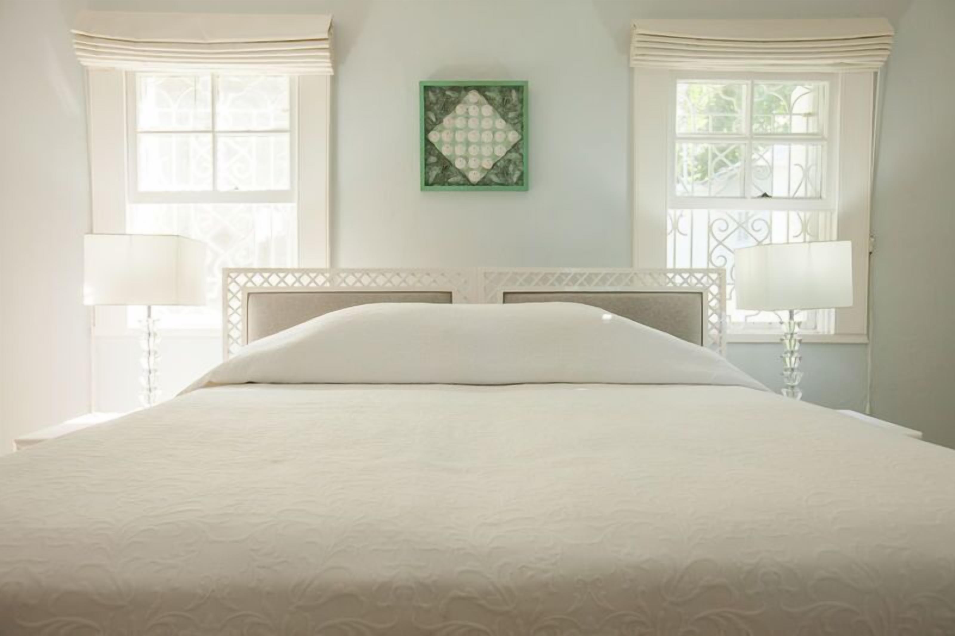 A neatly made bed with a headboard, two bedside lamps, and a framed artwork on the wall.