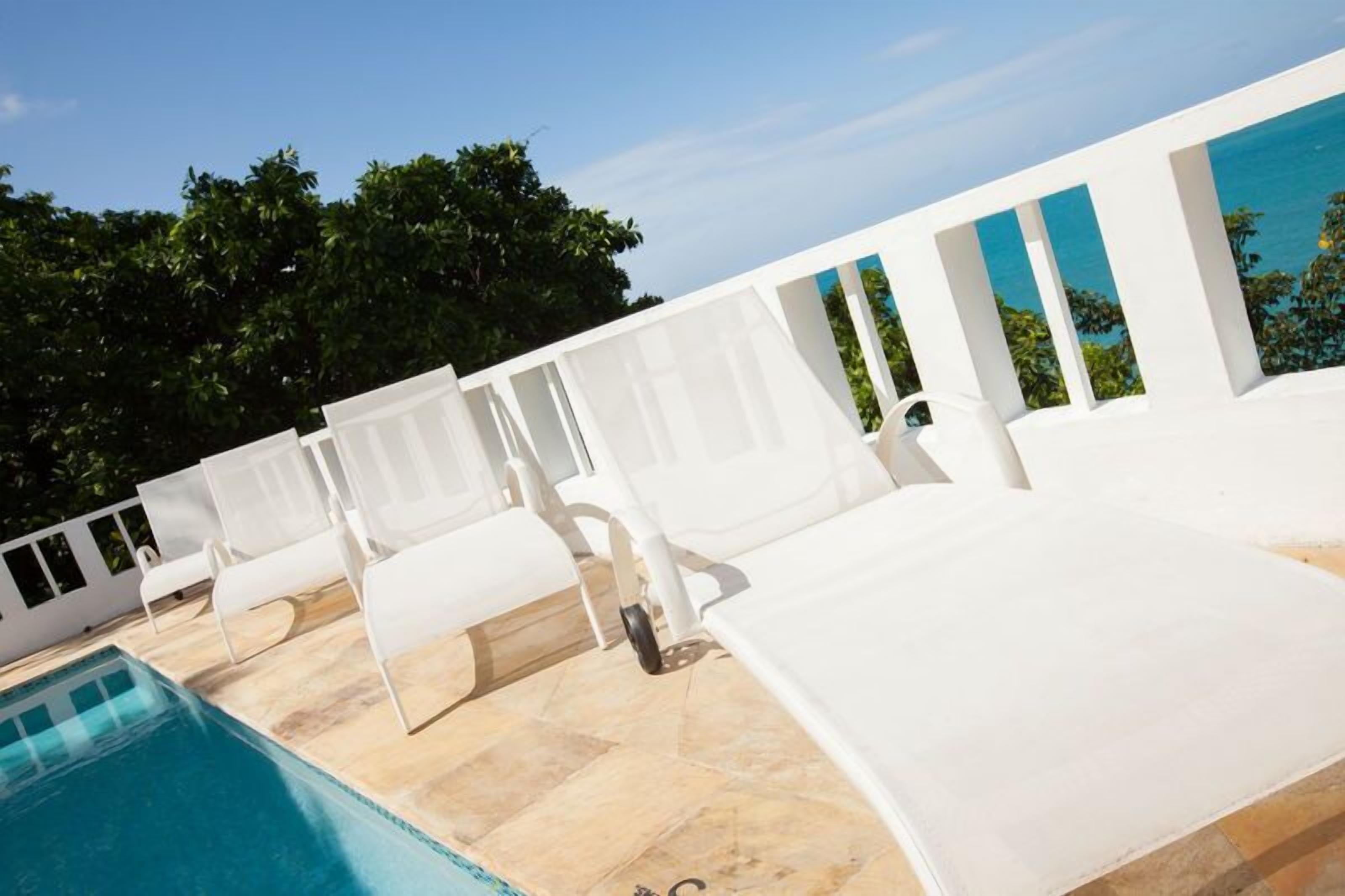 A poolside area with white lounge chairs and a clear view of the ocean.