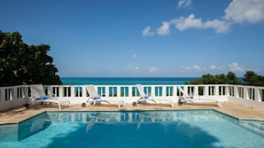 A pool with lounge chairs and a white fence overlooking a clear blue sea. - Wag Water Villa, Ocho Rios 3BR (Ocho Rios)