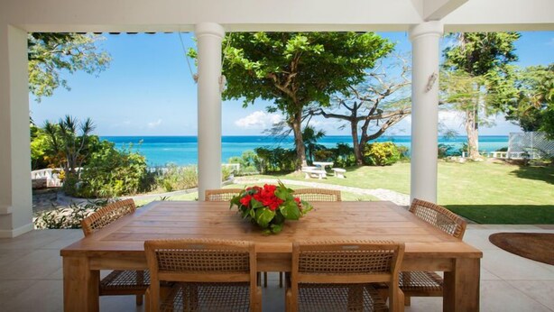 A covered outdoor dining area with a view of the ocean, surrounded by white columns and lush greenery. - Wag Water Villa, Ocho Rios 3BR (Ocho Rios)