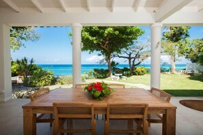 A covered outdoor dining area with a view of the ocean, surrounded by white columns and lush greenery. - Wag Water Villa, Ocho Rios 3BR (Ocho Rios)