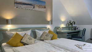 A hotel room with a bed, a desk, and a chair. There is a painting on the wall and a vase with flowers on the desk. - Hotel Residenz Lauterbach  (Putbus)
