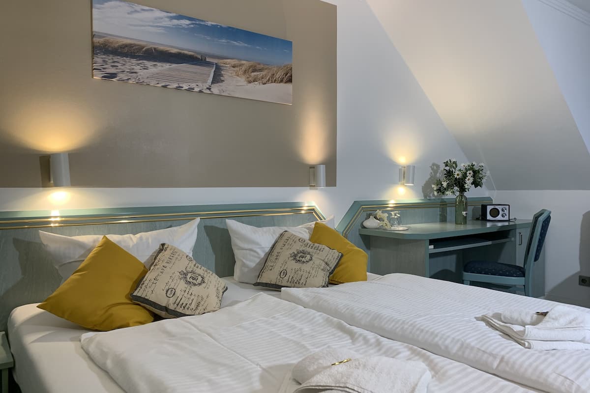 A hotel room with a bed, a desk, and a chair. There is a painting on the wall and a vase with flowers on the desk.