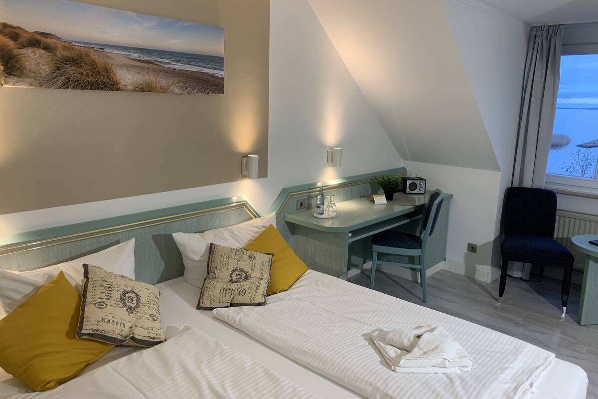 A hotel room with a bed, a desk, a chair, a radio, and a painting of a beach scene.