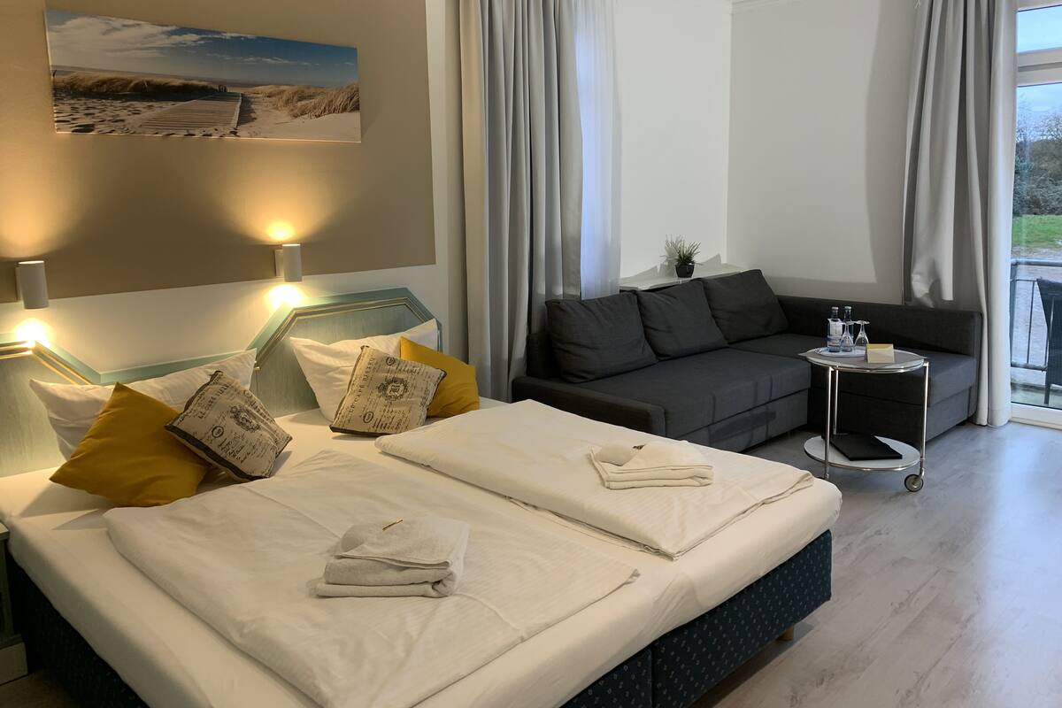 A hotel room with a bed, a sofa, a small table with a tray, and a view of the outdoors.
