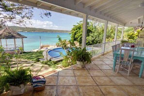 Une terrasse couverte avec une piscine, du mobilier d’extérieur et une vue sur la mer.