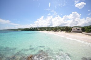 A beach with clear turquoise water, a sandy shore, and a small building with a tiled roof. - Sea Wyf Cottage, Silver Sands 2BR (Duncans)