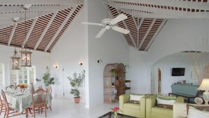 A spacious living area with a high ceiling, a dining table set for four, a green sofa, and a television.