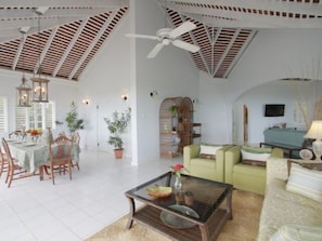 A spacious living area with a high ceiling, a dining table set for four, a green sofa, and a television. - Serendipity, Montego Bay 5BR (Montego Bay)