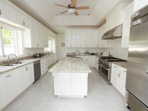 A modern kitchen with white cabinetry, a central island, stainless steel appliances, and a ceiling fan. - Serendipity, Montego Bay 5BR (Montego Bay)