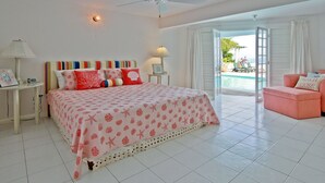 A bedroom with a bed, a ceiling fan, a nightstand, a lamp, a framed picture, and a view of a pool through an open door.