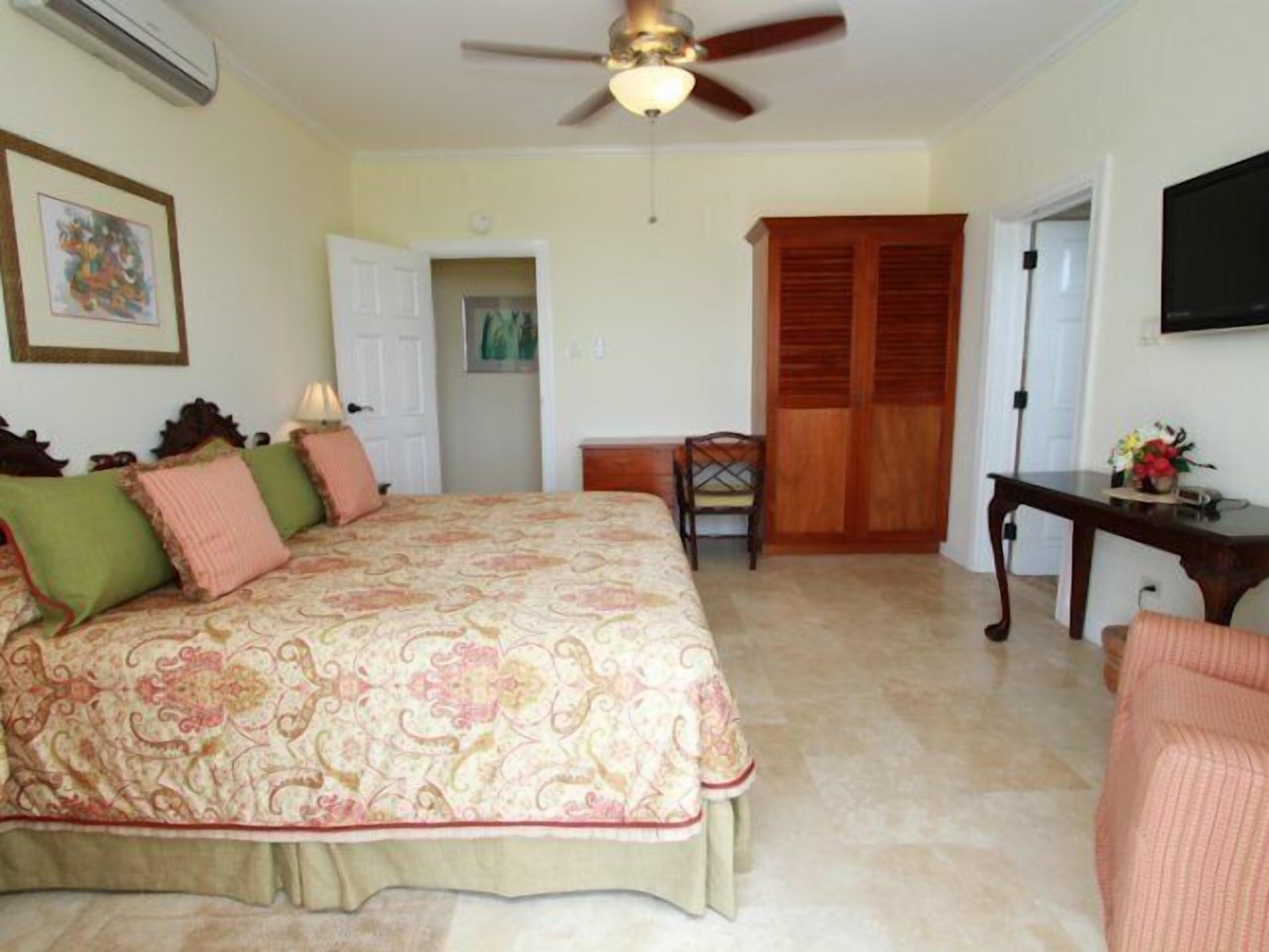 A bedroom with a bed, a desk, a chair, a wardrobe, and a ceiling fan.