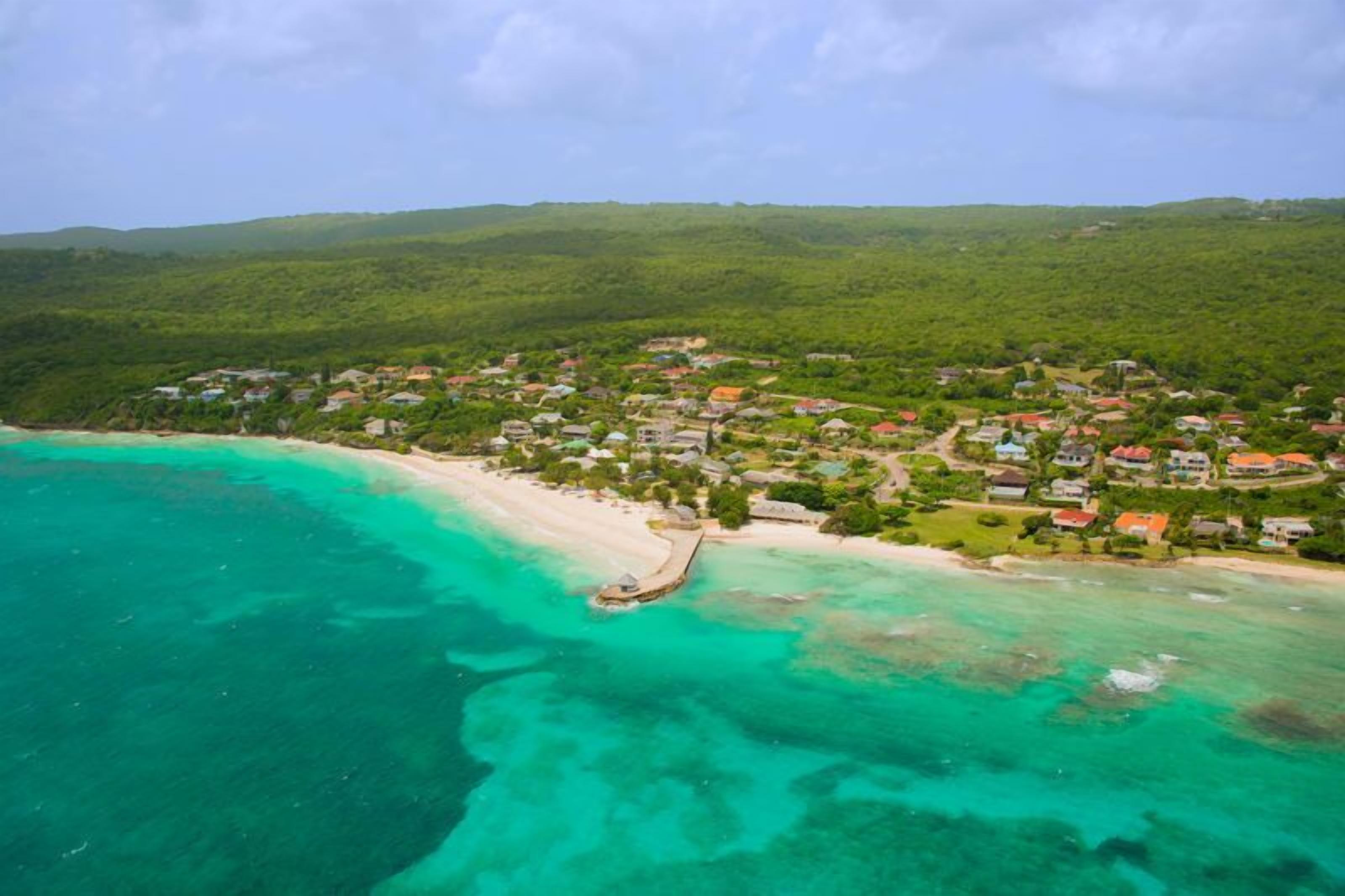 An aerial view of a coastal resort with beachfront properties, clear turquoise waters, and lush greenery.