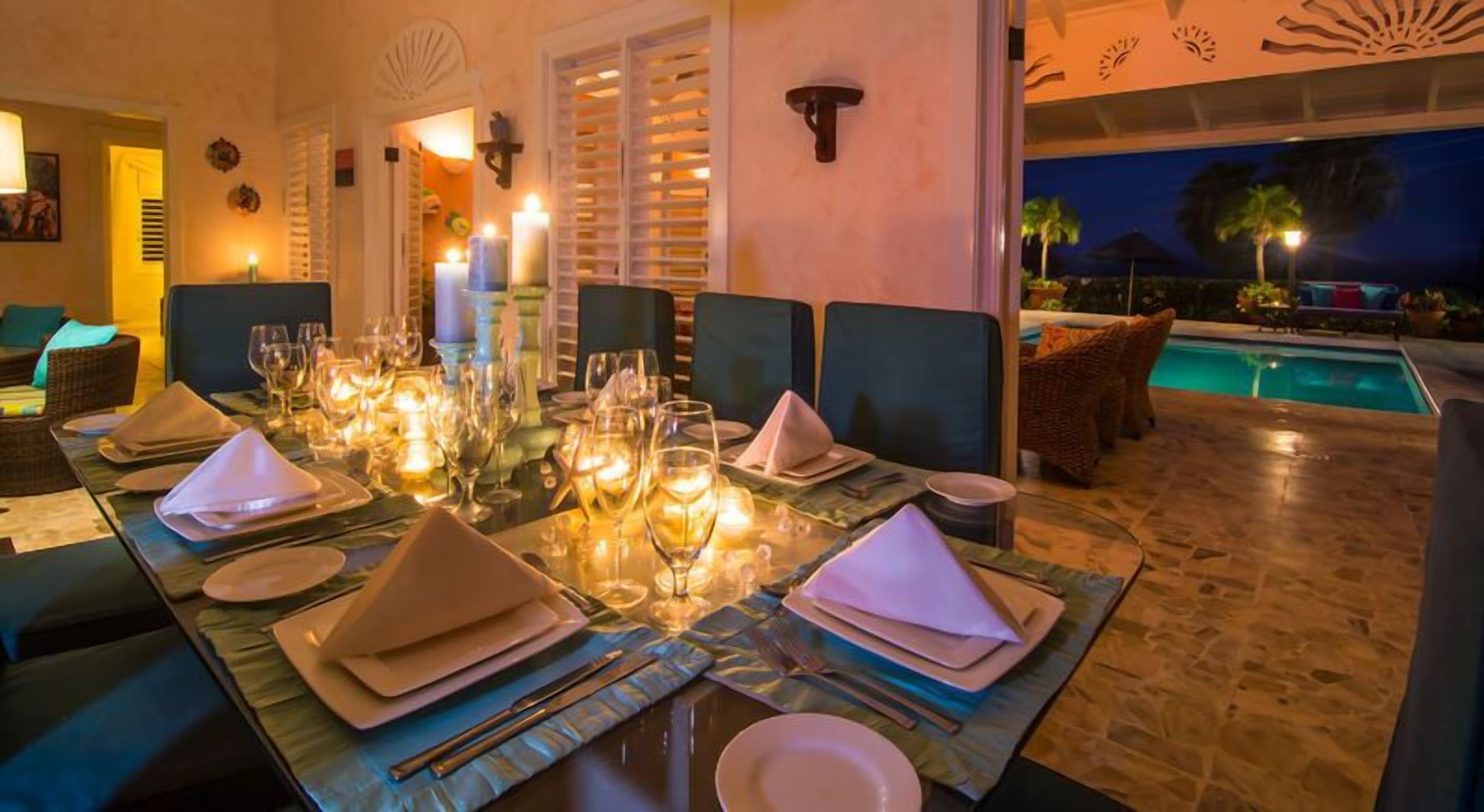 Un comedor con una mesa dispuesta para seis personas, rodeado de sillas de mimbre, y una piscina visible al fondo.
