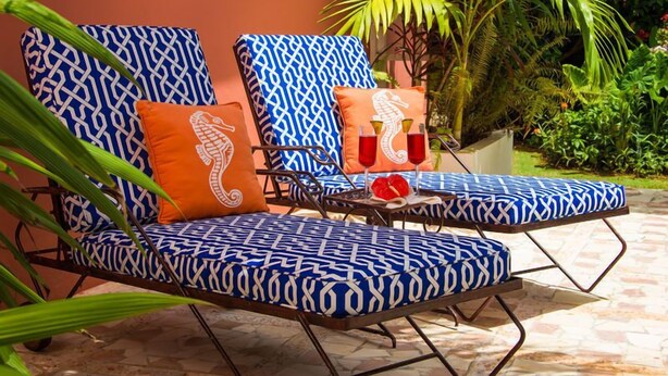 Two lounge chairs with blue patterned cushions and orange pillows, placed on a tiled patio with a palm tree and greenery in the background. - Summertime, Silver Sands,4BR (Duncans)