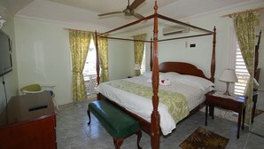 A four-poster bed with a wooden frame, a green bench, a desk with a computer, and a ceiling fan. - Sol Mar, Silver Sands 3BR (Duncans)