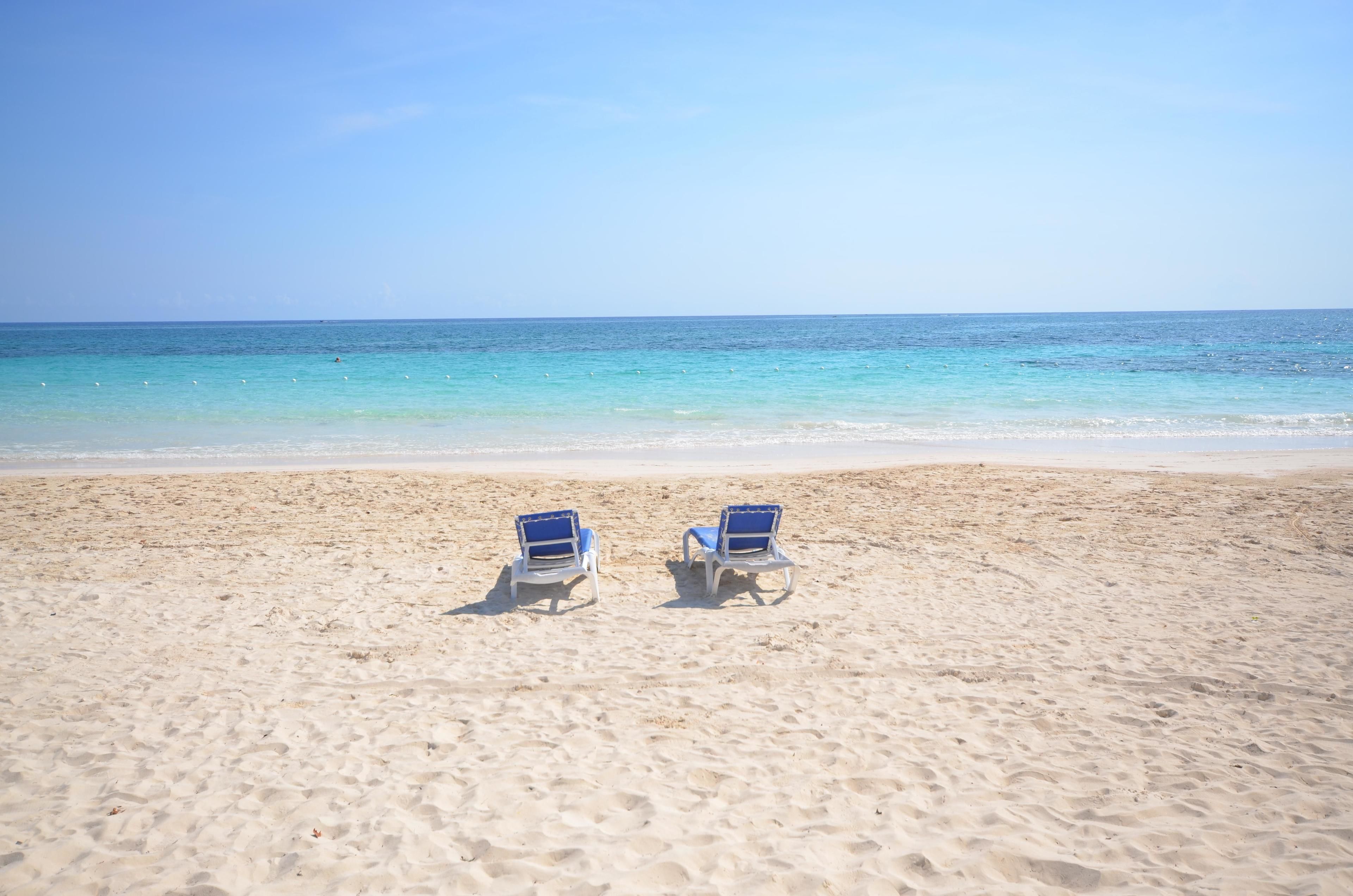 A beach with two blue beach chairs facing the ocean.