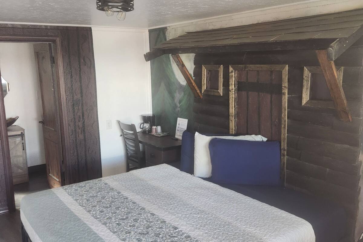 Una habitación con cama, escritorio, silla, microondas y refrigerador pequeño.