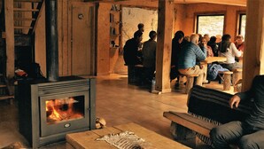 A cozy room with a wood-burning stove, a map on the wall, and a group of people gathered around a table. - Puesto Cagliero refugio de montaña (El Chalten)