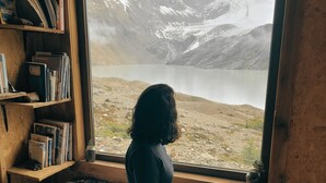 A person sitting by a window overlooking a mountainous landscape. - Puesto Cagliero refugio de montaña (El Chalten)