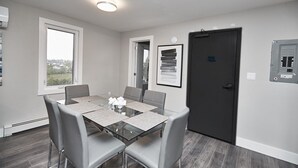 A modern dining area with a glass table, grey chairs, and a dark door. - Clifton Hill Condo's (Niagara Falls)