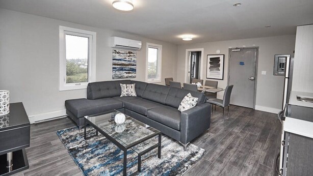 A modern living room with a sectional sofa, a coffee table, and a dining area with a table and chairs. - Clifton Hill Condo's (Niagara Falls)
