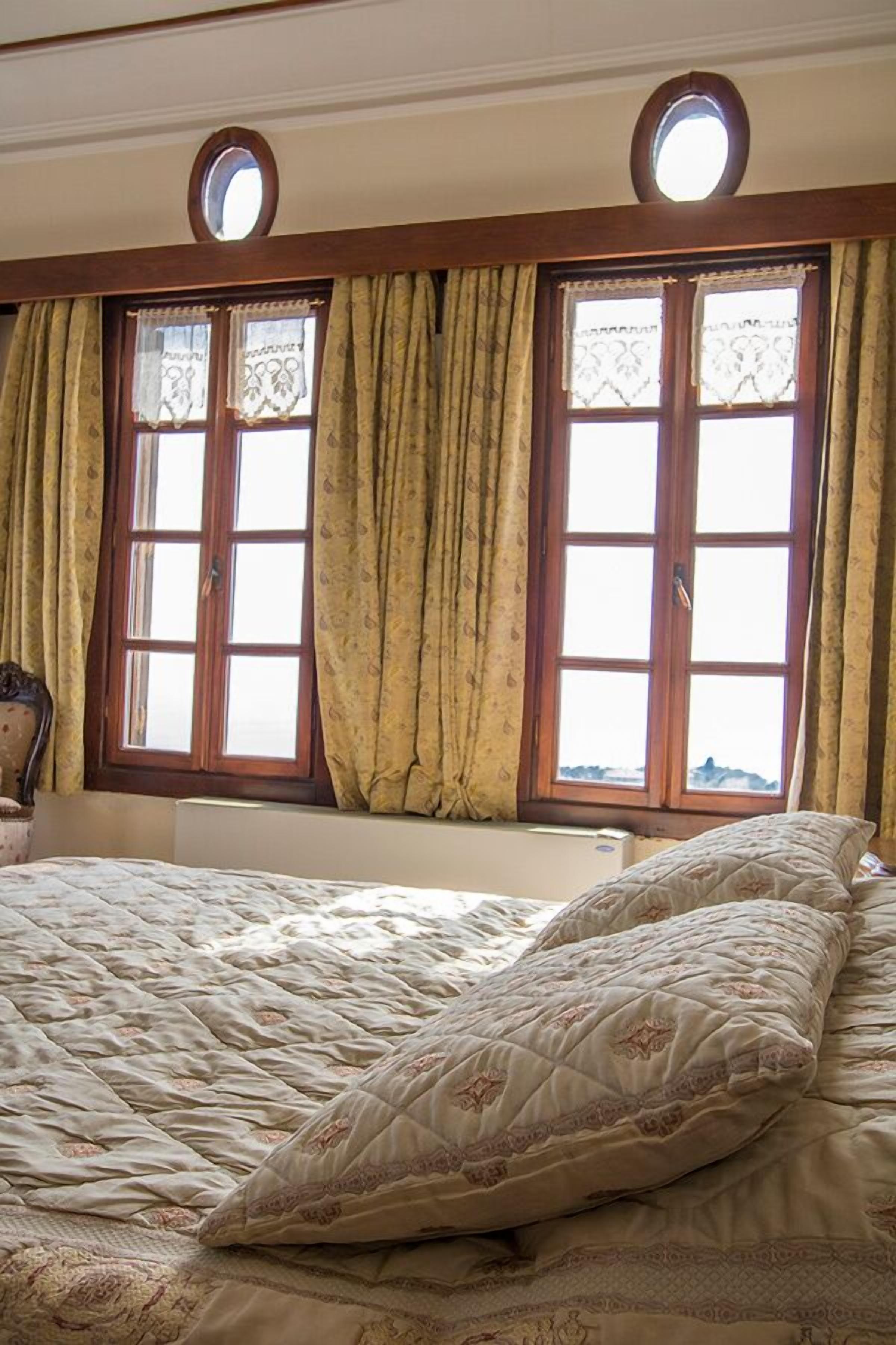 A bedroom with a large bed, two windows with curtains, and a small round window above the bed.