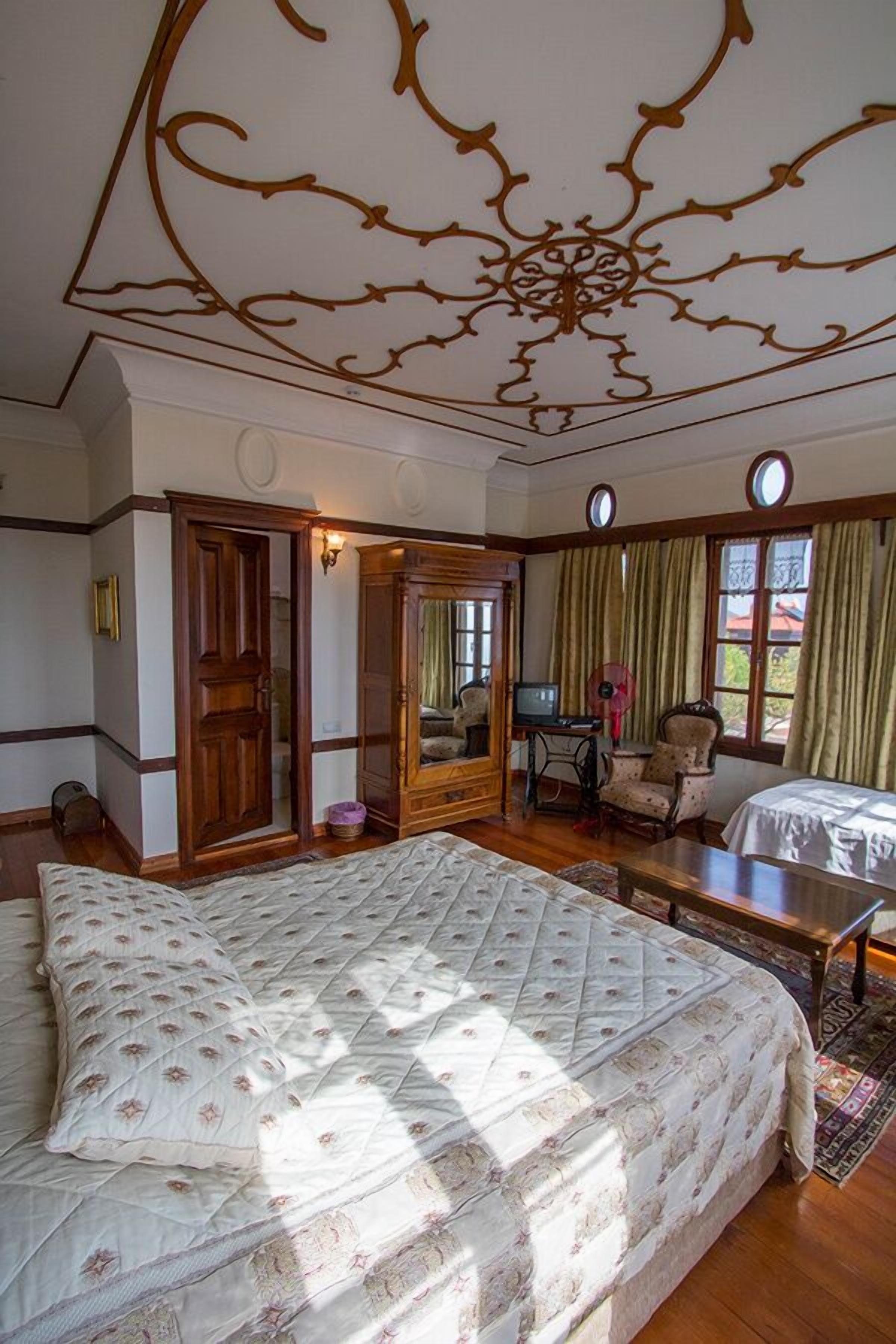 Un dormitorio con una cama grande, un armario de madera, una máquina de coser y una silla.