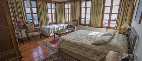 Un dormitorio amplio con una cama grande, dos sillones, una mesa y varios ventanales con cortinas.