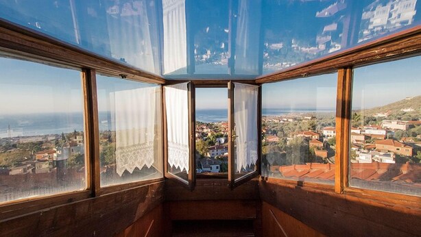 A corner room with large windows offering a view of a coastal town and the sea.