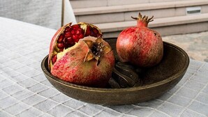 A pomegranate on a plate on a table outside a building with stone walls and wooden doors.