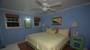 A bedroom with a bed, two bedside tables, a ceiling fan, and artwork on the walls. - San Cove, Blue Lagoon, Port Antonio 4BR (Port Antonio)