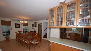 A dining area with a wooden table and chairs, a kitchen with wooden cabinets and a stainless steel refrigerator, and a staircase leading to another level. - San Cove, Blue Lagoon, Port Antonio 4BR (Port Antonio)