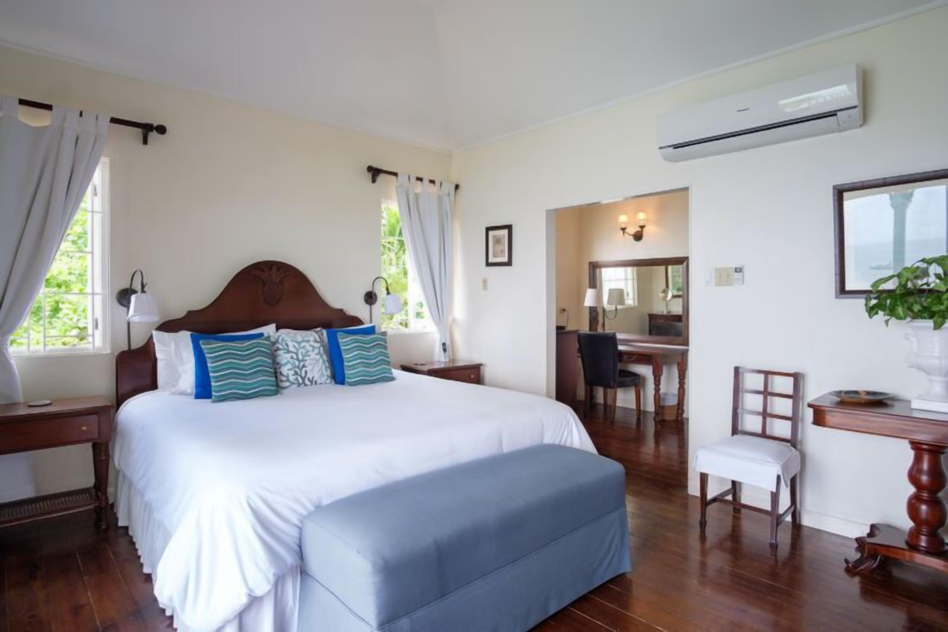 A bedroom with a large bed, a wooden headboard, a desk with a chair, and an air conditioning unit.