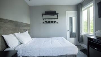 A modern hotel room with a neatly made bed, a wall-mounted coat rack, and a large window providing a view of the outdoors.