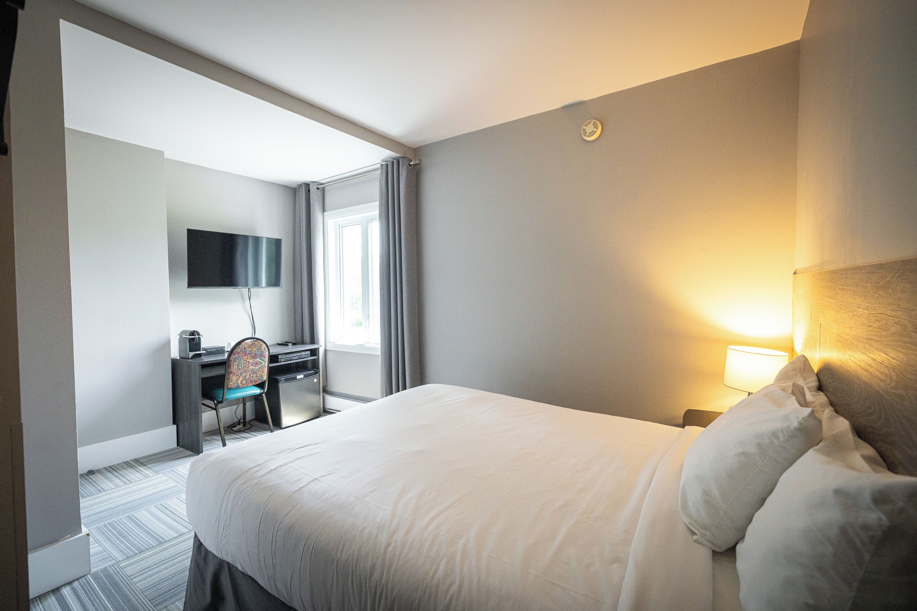 A hotel room with a large bed, a desk with a chair, a flat-screen TV, and a bedside lamp.