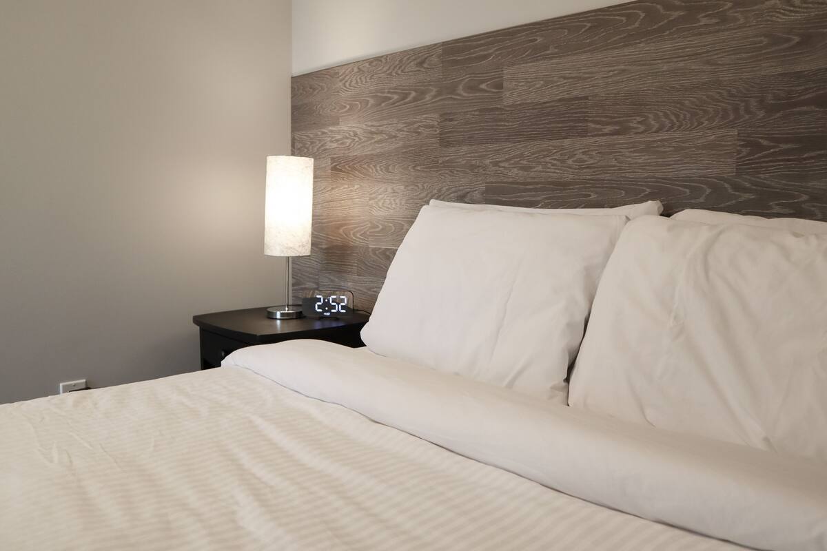 A neatly made bed with white linens, a bedside lamp, and a digital clock displaying 2:52.