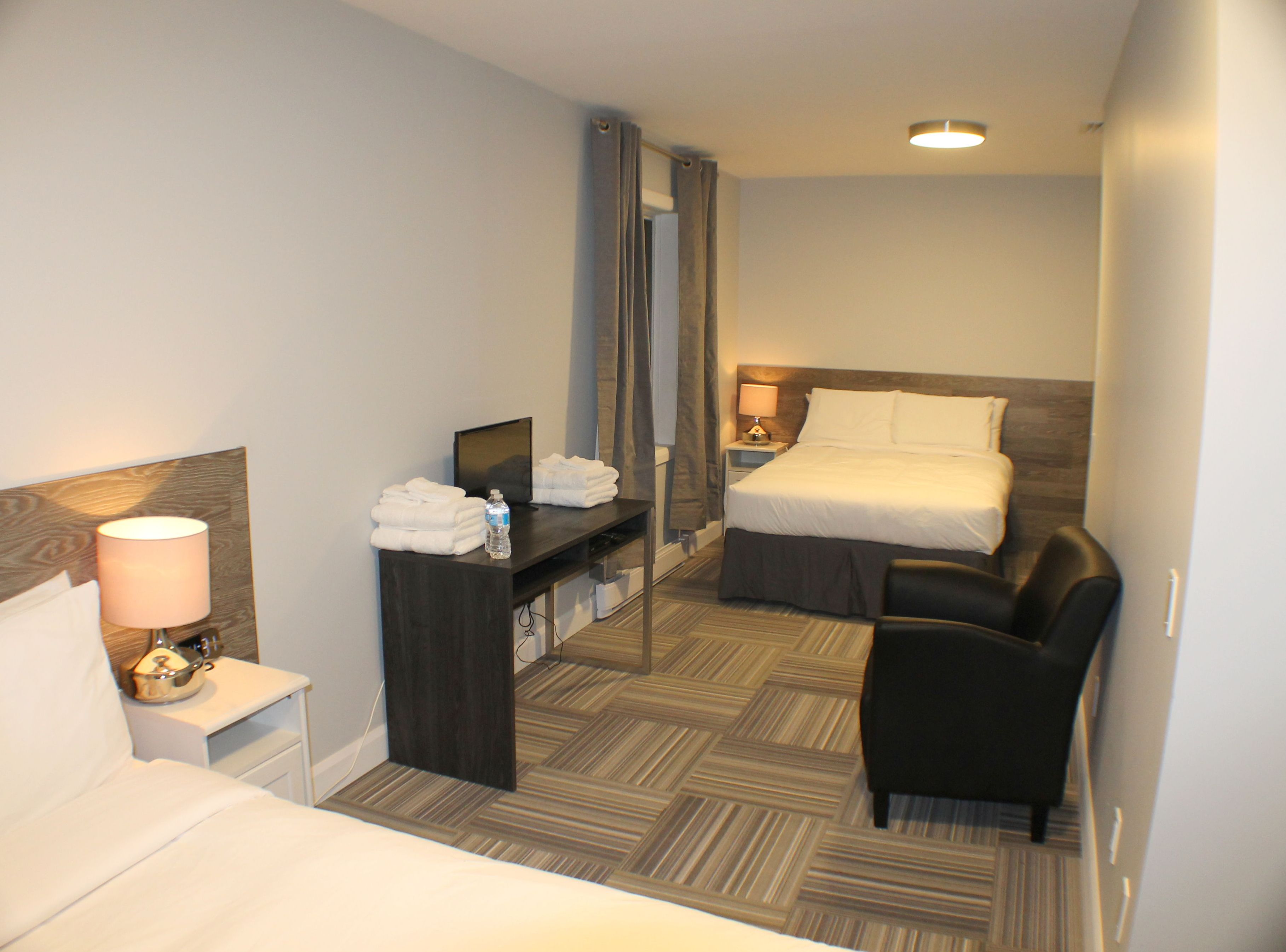 Una habitación de hotel con una cama, un escritorio con lámpara, una silla y un espejo.