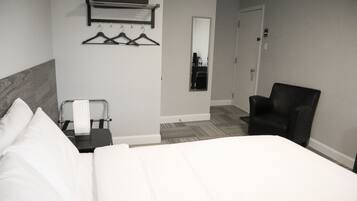 A hotel room with a bed, a chair, a mirror, and a coat rack with hangers.
