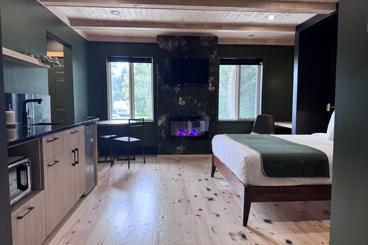 A bedroom with a bed, a fireplace, a desk, and a kitchen area.