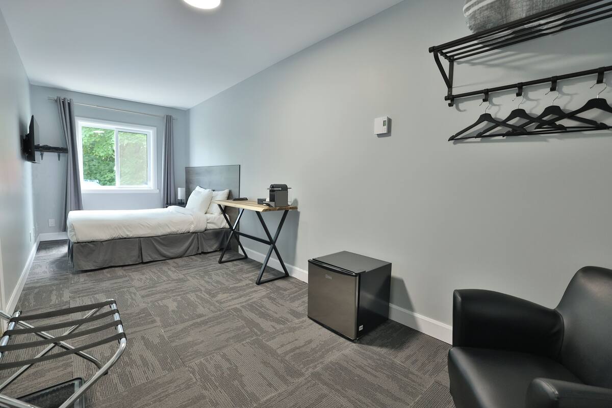 A modern hotel room with a bed, desk, chair, and a small refrigerator.